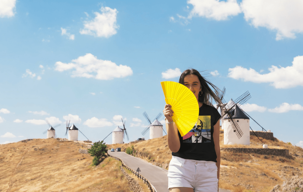 Дівчина у чорній футболці EvilDOC із жовтим віялом на фоні вітряків